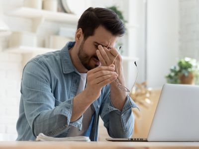 Mann vor Laptop sitzen mit Kopfschmerzen